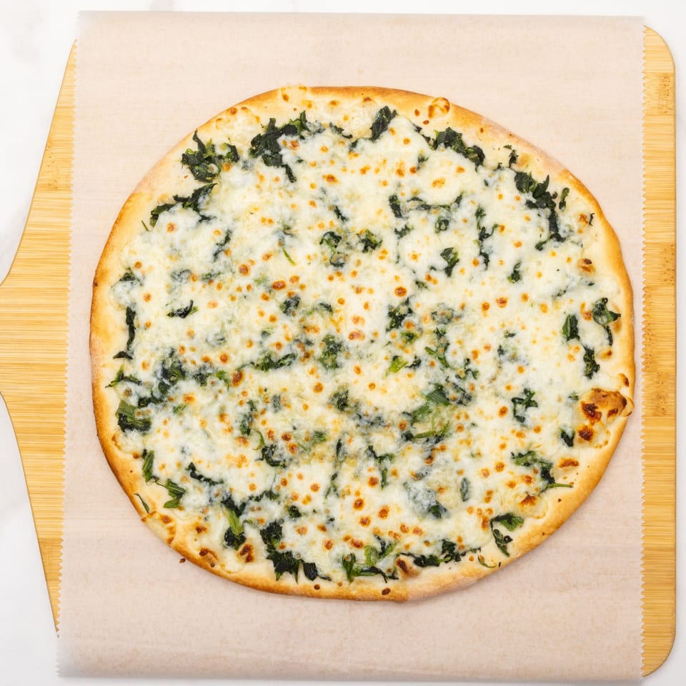 A white pizza with spinach and melted cheese on a wooden pizza peel.