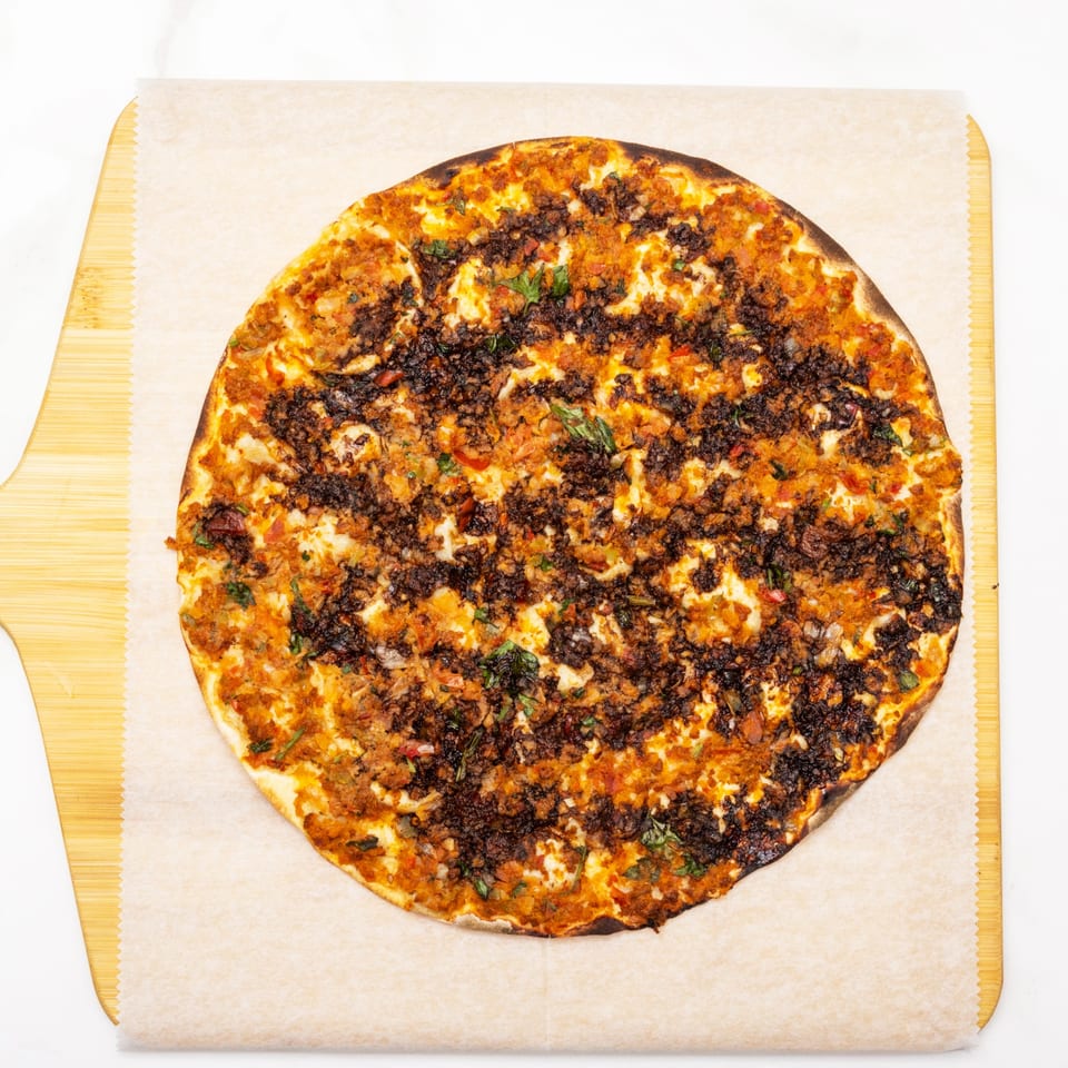 Overhead view of a round, savory flatbread with dark, crumbled meat and herbs on parchment paper.