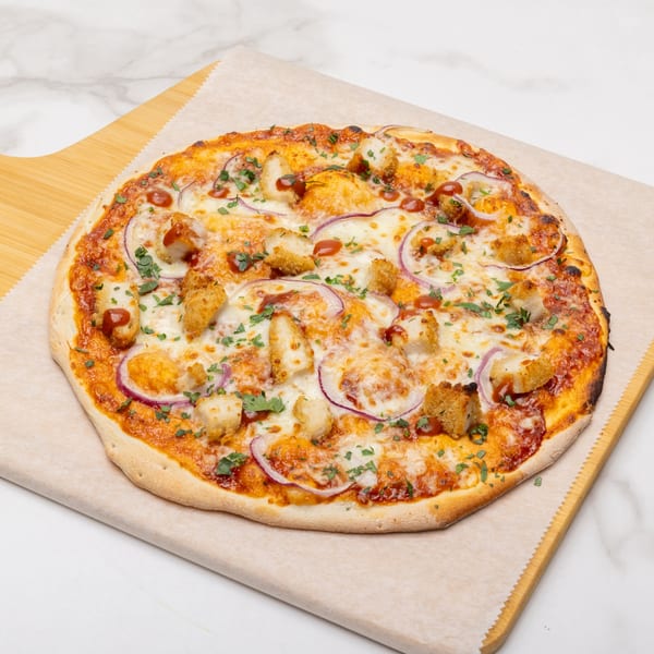 BBQ chicken pizza with red onions, cilantro, and a drizzle of barbecue sauce on a wooden peel.