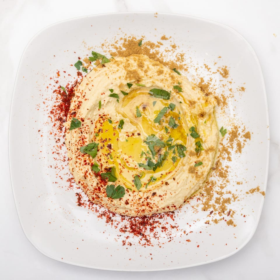 Creamy hummus drizzled with olive oil, garnished with parsley, paprika, and cumin on a white plate.