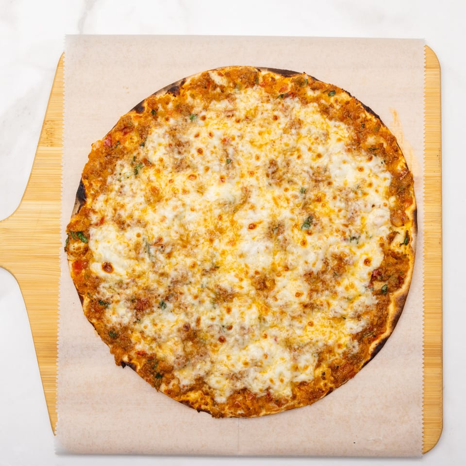 A round, cheesy pizza with a rich red sauce and golden crust, served on parchment paper on a wooden peel.