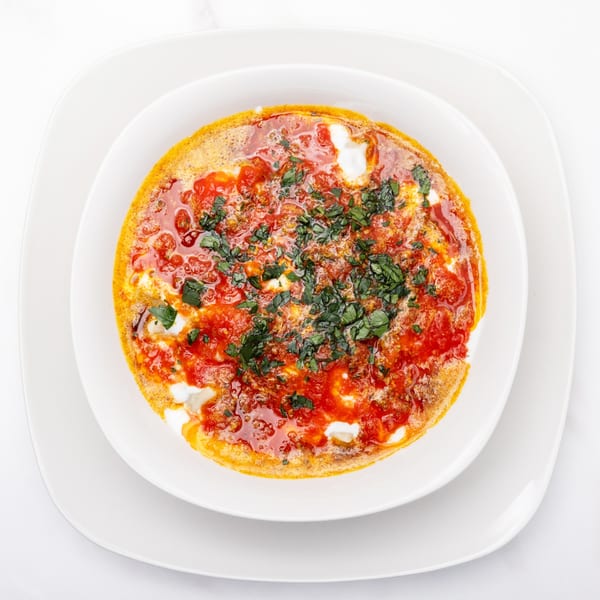 Overhead view of a white bowl filled with shakshuka, garnished with fresh herbs.