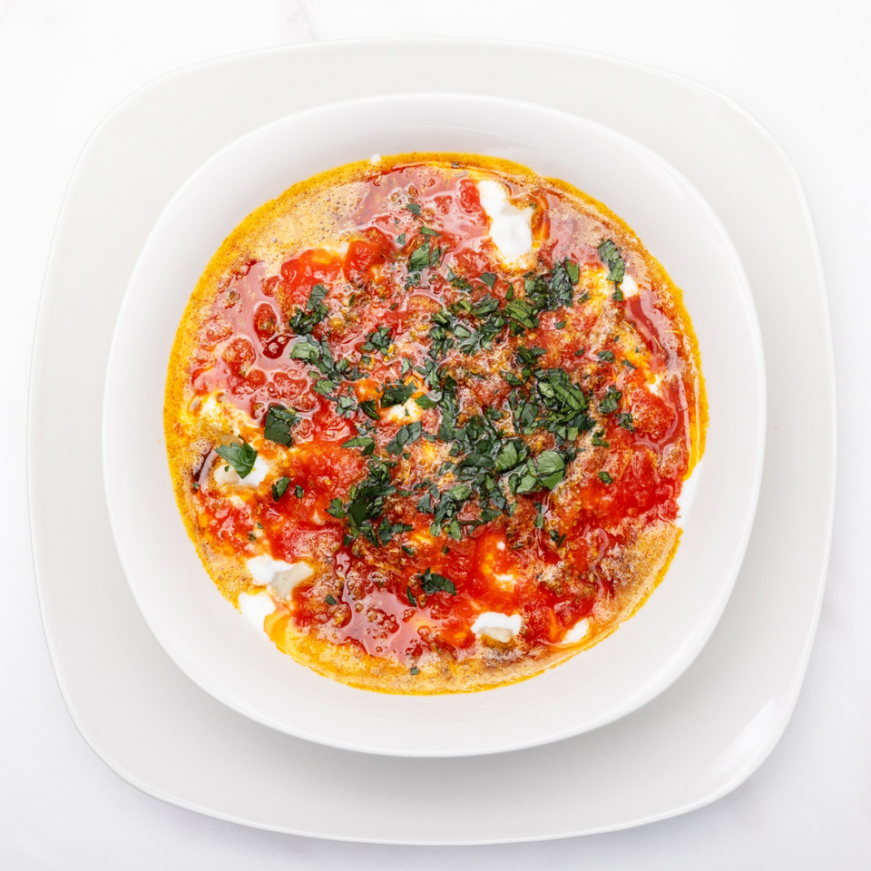 Overhead view of a white bowl filled with shakshuka, garnished with fresh herbs.