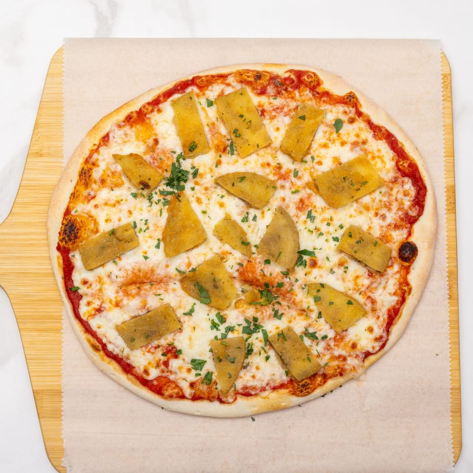 A round pizza with melted mozzarella, tomato sauce, fried polenta squares, and fresh parsley on a wooden board.